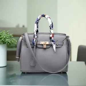 Grey textured leather handbag detail view, metal padlock and chic silk scarf decoration.