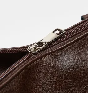 Close-up detail shot of a brown leather bag zipper and smooth metallic hardware texture.