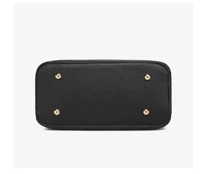 Close-up detail of black leather handbag bottom with four gold metal protective feet.