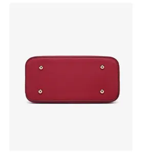 Red handbag bottom detail, featuring four gold metal protective feet and clean leather texture.
