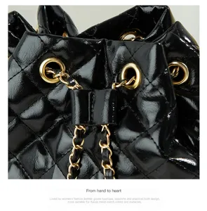 Close-up detail view of black quilted patent leather bucket bag with gold chain grommets.