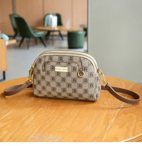 Detailed view of the stylish monogram crossbody shell bag with double zipper and brown strap.