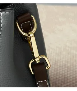 Detail view of women's leather shoulder bag hardware, featuring gold clasp and dark brown strap.