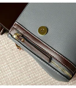 Close-up detail of stylish color-blocked leather handbag with zipper and magnetic snap closure.