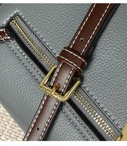 Close-up detail of stylish grey leather handbag showing brown straps, metal buckle and zipper.