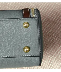 Grey leather handbag detail showing gold metal feet and stitching, elegant accessory close up.