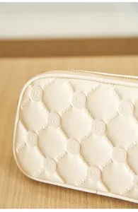 Cream white quilted cosmetic bag with elegant debossed monogram letters and zip closure.