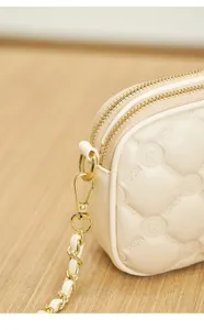 Detailed view of quilted beige crossbody bag with gold chain strap and dual zippers.