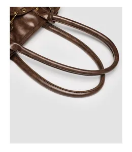 Close-up detail of retro brown leather handbag handle with metal eyelets and fine stitching.