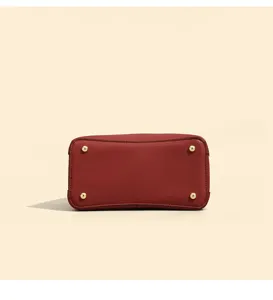 Red leather handbag bottom detail showcasing gold metal feet and fine texture craftsmanship.