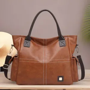 Detailed view of brown leather tote bag with cross stitching, handles, and strap.
