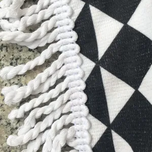 Detailopname van ronde strandhanddoek, zwart-wit geometrisch patroon met kwastjesrand.