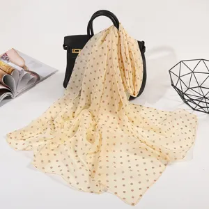Detail view of a light yellow polka dot silk scarf draped on a chic black handbag for spring.