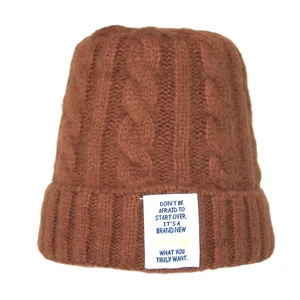 Détail de bonnet en tricot torsadé marron avec étiquette textuelle en anglais motivante.