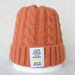 Gros plan détaillé du bonnet en tricot torsadé orange avec écusson textuel blanc.