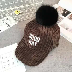 Corduroy baseball cap featuring fluffy black pom-pom and stylish white letter embroidery detail.