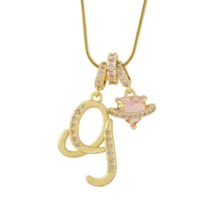 Gros plan d'un collier pendentif lettre dorée et cœur rose planète avec des zircons brillants.