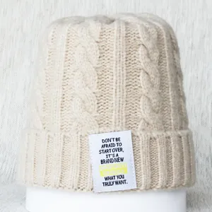Gros plan d'un bonnet en tricot beige avec un patch de texte citation motivante.