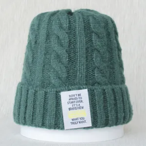 Gros plan sur un bonnet en tricot torsadé vert foncé avec patch de texte inspirant.