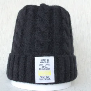 Vue détaillée du bonnet en tricot torsadé noir avec un patch de texte inspirant.
