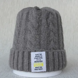 Détail du bonnet en tricot gris avec un patch tissé blanc et une citation inspirante.
