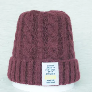 Bonnet en tricot bordeaux pour femme avec motif torsadé chaud et patch de citation inspirant.