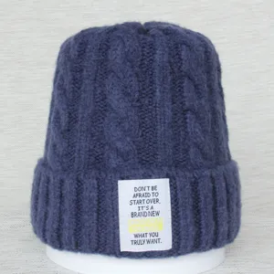 Bonnet en tricot détail, motif torsadé bleu foncé, étiquette tissée blanche avec citation.