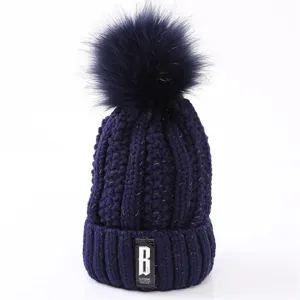 Winter warm navy blue knitted beanie hat with fluffy pom pom and stylish front label.