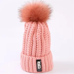 Cute pink knitted winter beanie hat with big fluffy pom-pom and stylish front label detail.