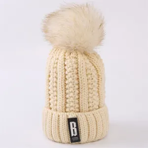 Close up detail of a cozy beige knitted winter beanie hat with a fluffy faux fur pom pom.