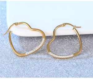 Detailaufnahme von stylischen goldenen Edelstahl-Herz-Creolen mit Kristallbesatz.