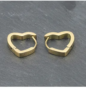 Nahaufnahme von minimalistischen goldenen Edelstahlohrringen in Herzform auf dunklem Schiefer.