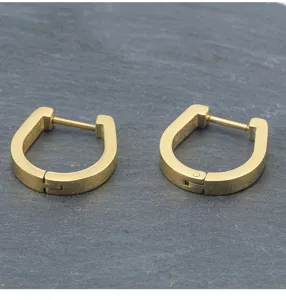 Primer plano detallado de pendientes de aro ovalados lisos de acero inoxidable dorados.