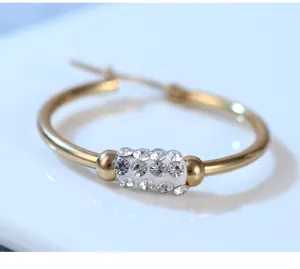 Primer plano detalle de pendiente de aro dorado con elemento de cuenta blanca con pavé de cristal.
