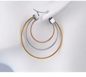 Close-up detail of minimalist three-layer hoop earrings in gold silver and rose gold tones.