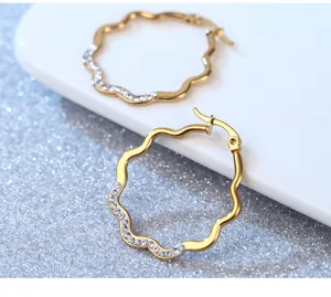 Close-up detail view of luxury gold wavy hoop earrings featuring paved sparkling micro crystals.