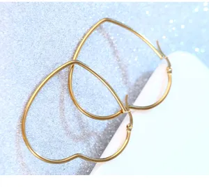 Detailansicht filigrane herzförmige Edelstahl-Ohrringe in Gold, minimalistischer Stil.