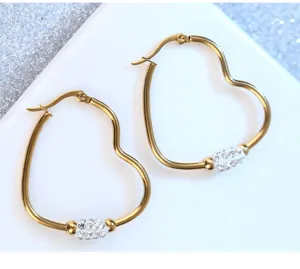 Primer plano de pendientes de aro dorados en forma de corazón con pedrería blanca brillante