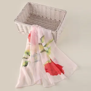 Detailopname van een lichte roze chiffon sjaal met rode rozenprint en groene bladeren.