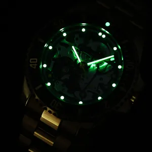 Detalle de reloj mecánico luminoso con esfera esqueleto y manecillas verdes oscuras.