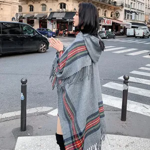 Detailed view of grey hooded plaid shawl cape with fringe and striped pattern in street scene.