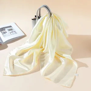 Elegant light yellow silk satin scarf draped elegantly, soft glossy fabric texture detail.
