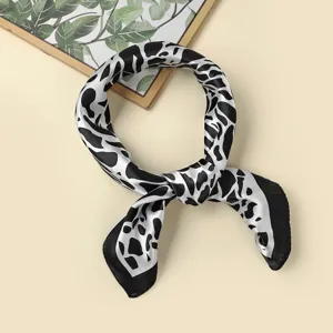 Close-up view of the black and white abstract print square silk scarf, neatly knotted.