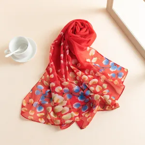 Vue détaillée d'un foulard imprimé floral rouge, élégamment roulé, idéal pour la plage et l'été.