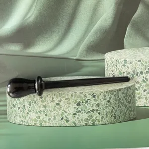 Detail shot of black silicone eyeliner tool on green terrazzo podium and fabric backdrop.