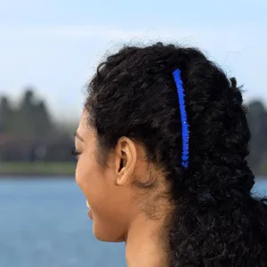 Detail view of a vibrant blue banana hair clip worn on curly hair, outdoors near water.