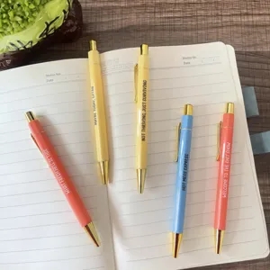 Close-up detail of colorful funny quote metal ballpoint pens neatly arranged on a notebook.
