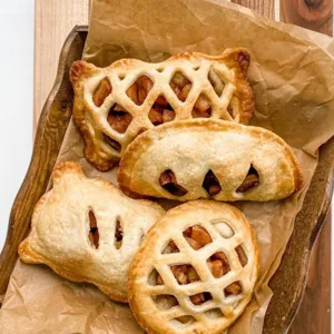 Close-up of freshly baked mini hand pies with classic lattice and crust designs on paper.