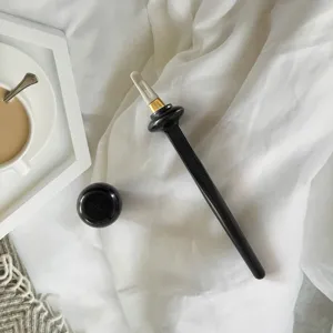 Close-up of black silicone eyeliner brush with gold detail and cap on white fabric.