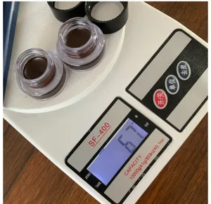 Detail view of gel eyeliner pots on digital scale showing net weight for quality control.